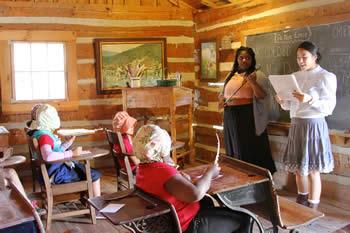 From left: Stephen F. Austin State University elementary education majors Brinisha Shaw and Holly Franz experience life as a teacher in the 1900s as they teach third graders a reading lesson in a one-room schoolhouse at Millard’s Crossing Historic Village. This activity was part of the annual Pioneer Days event coordinated by SFA, Millard’s Crossing and area schools.