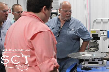 A crowd gathers as Michael Smith etches a design into the side of a saw blade using a laser.